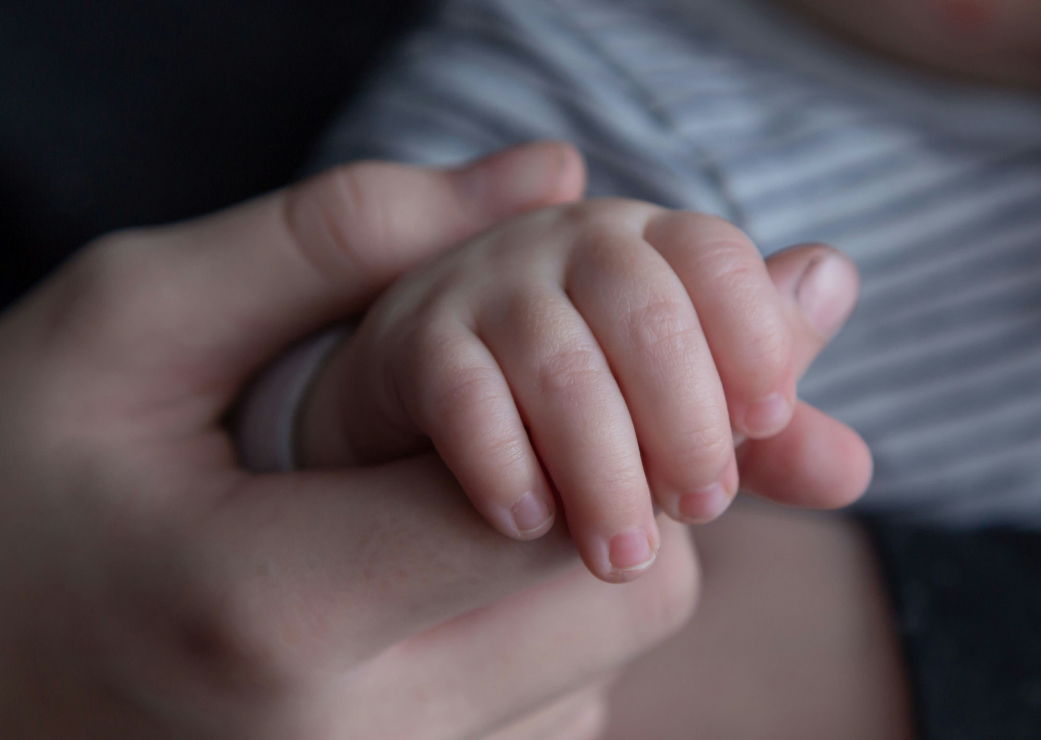 Baby's hand gently holding an adult's finger, showing tender comfort moment
